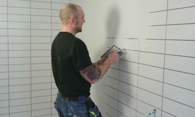 A man in a black shirt and blue pants tiling a bathroom.